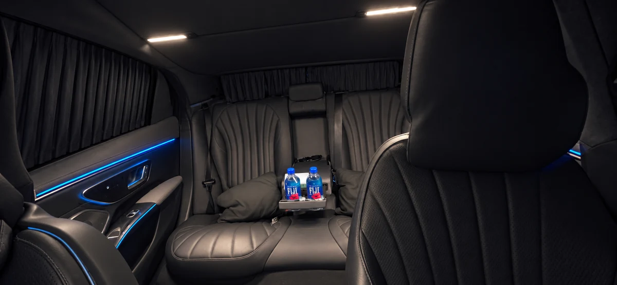 Rear cabin of Arion&rsquo;s 2023 Mercedes-Benz EQS 450 with black leather seating, blue ambient lighting and chilled water on the console