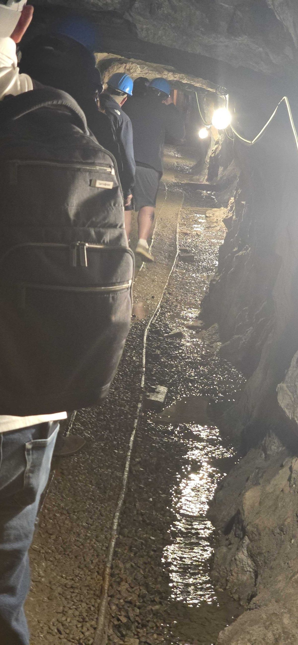 Visitors in blue hard hats walking through a narrow wet mine tunnel on the Lebanon Mine tour