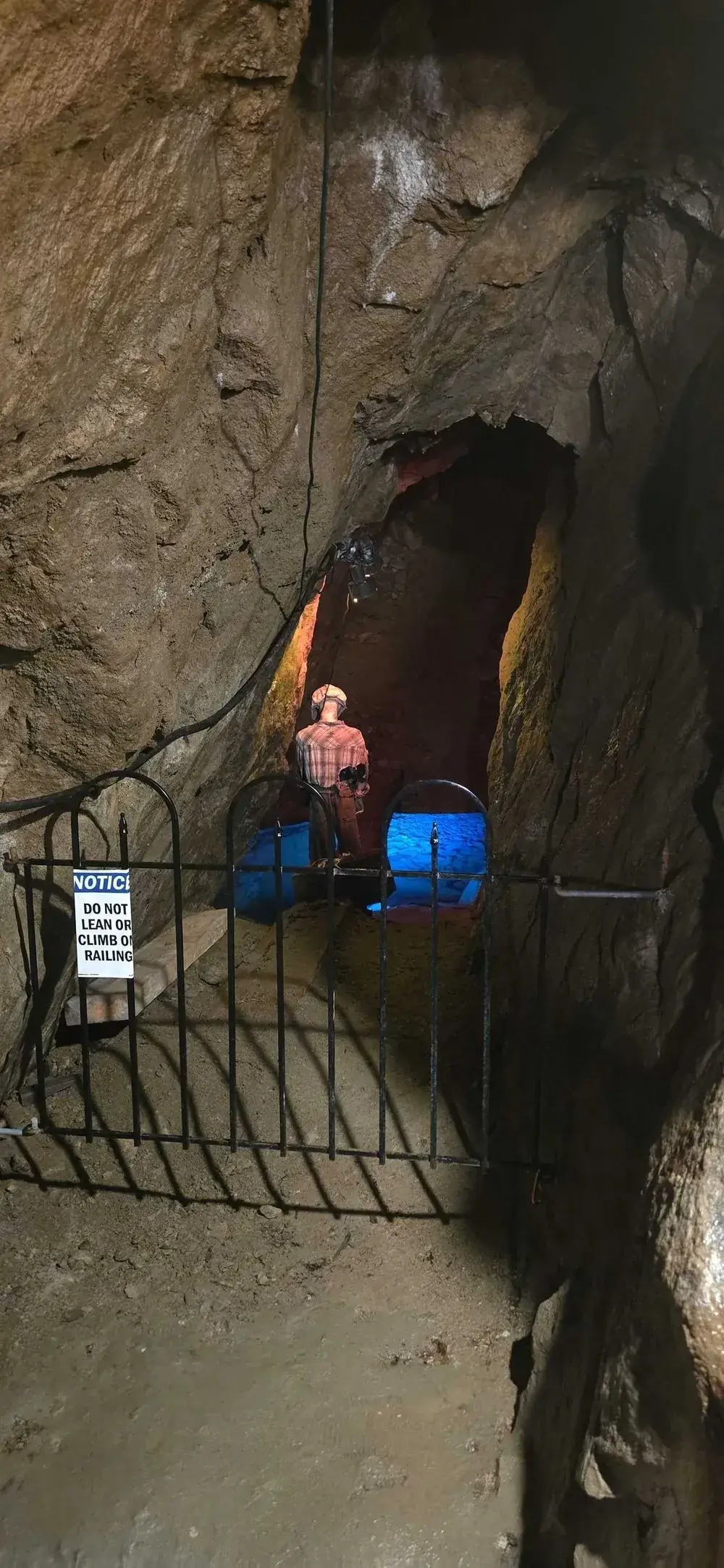 Mannequin of a miner in plaid shirt and hard hat standing near a blue-lit shaft