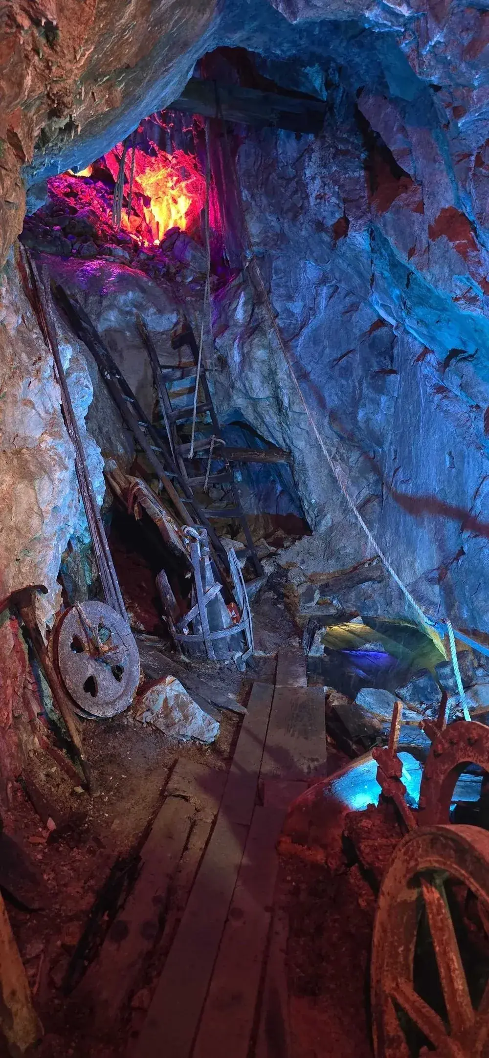 Original mining equipment inside a stope, ore cart wheels, ladders, and hoisting gear lit with colored lights