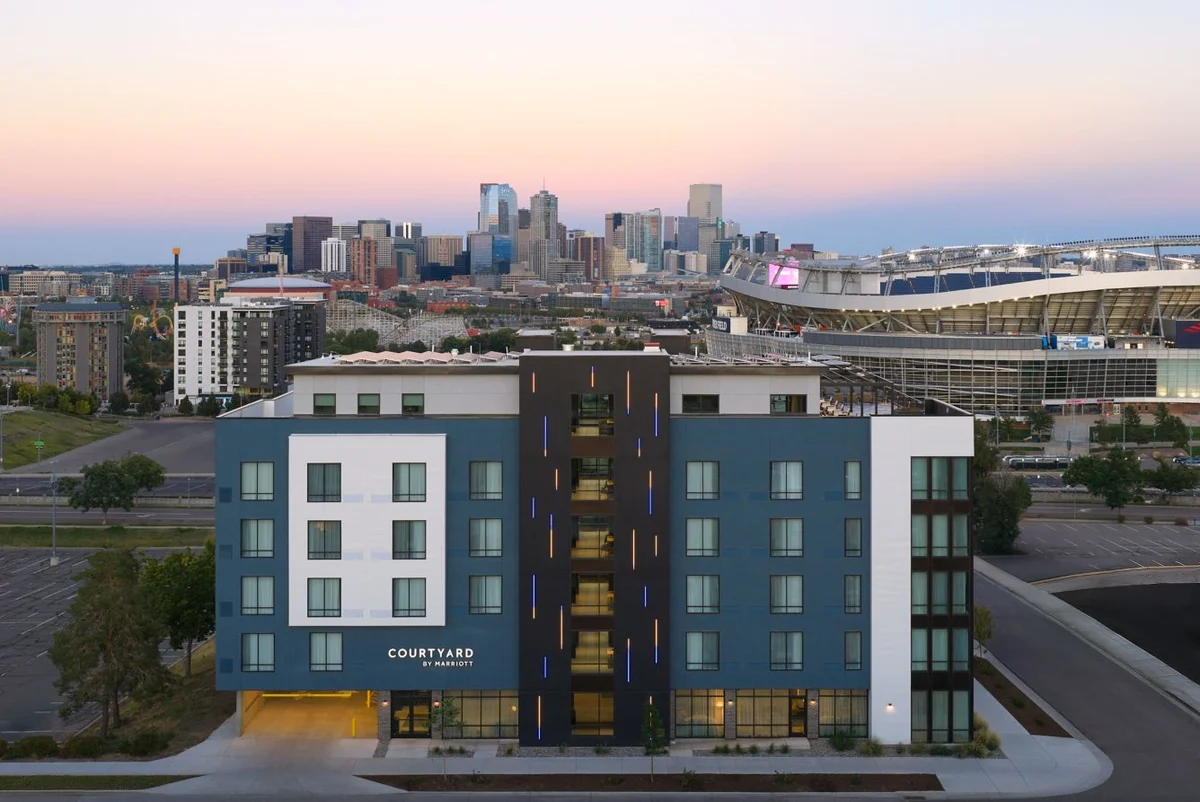 Courtyard by Marriott Denver Downtown West at dusk with the Denver skyline and Empower Field at Mile High behind it