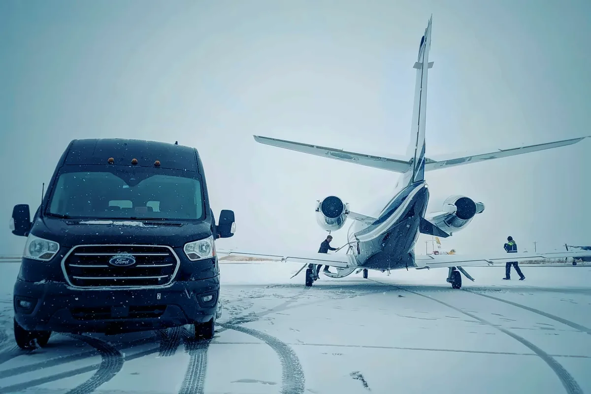 Black passenger van waiting on the snowy Atlantic Aviation ramp in Hayden behind a private jet